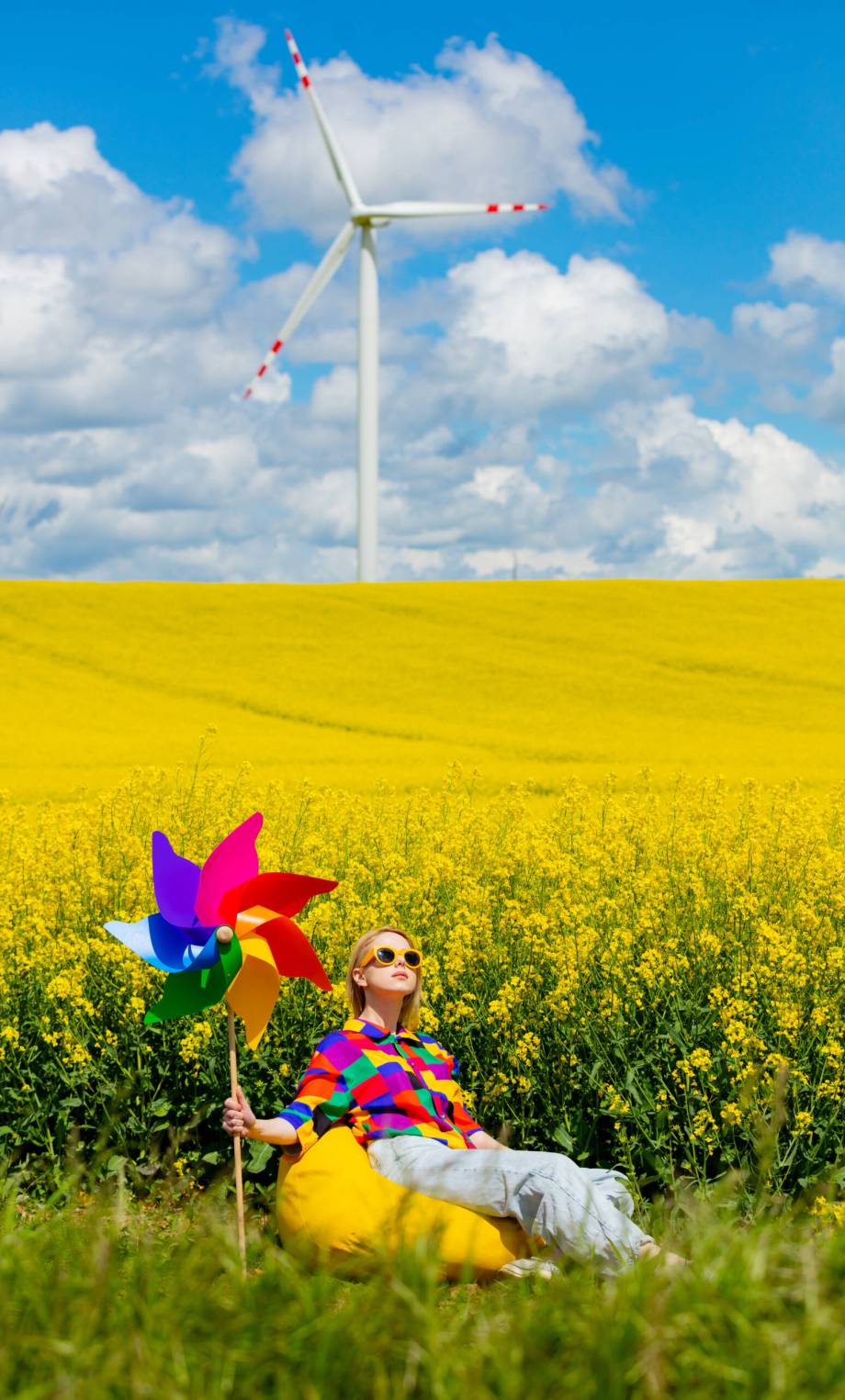 Beautiful female in 90s stylish shirt with pinwheel sitting in rapeseed field